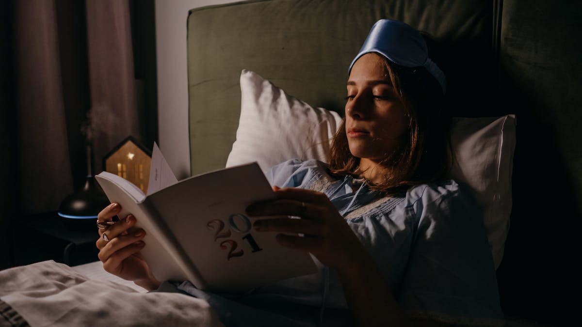 Woman in bed with sleep mask, reading a book, creating a relaxing, cozy atmosphere.